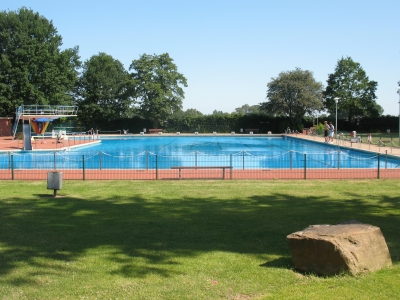 Das Freibad Mettingen. Außenanlage mit großer Rasenfläche und Bäumen im Hintergrund