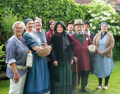 Die Sänger und Musiker für das Mettinger Heimatlied stehen vor einem Mikrofon im Garten. Sie sind in traditioneller Kleidung und lächeln in die Kamera.