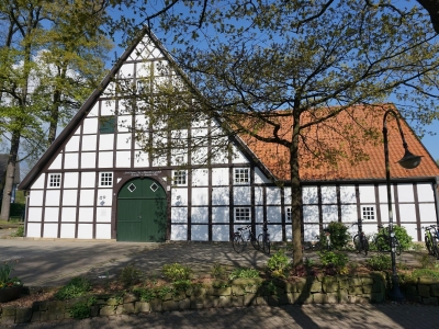 Außenansicht auf den Schultenhof Mettingen. Ein altes Fachwerkhaus mit weißer Front und hohem Dach mit roten Ziegeln.