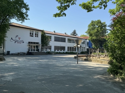 Außenansicht auf die Ludgeri-Schule Mettingen. Der Schulhof mit Spielgeräten und im Hintergrund das weiße mehrgeschossige Gebäude mit rotem Flachdach.