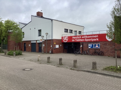 Blick von der Straße auf den Tüötten-Sportpark. Fahrradständer vor einer roten Klinkerwand. Ein mehrgeschossiges Gebäude