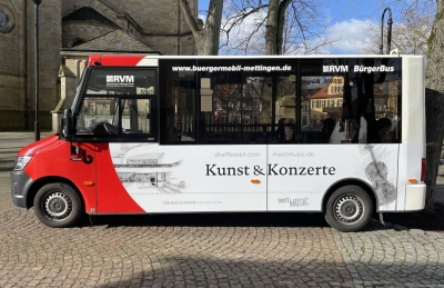 Ein Bild des Bürgermobil Mettingen. Seitenansicht. Der Kleinbus hat große Fenster und ist Weiß mit etwas Rot lackiert.