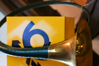 Mettinger Postmuseum Um einen gelben Briefkasten mit Post Logo ist ein altes Posthorn geschwungen.