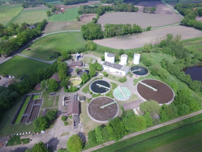 Außenansicht aus der Vogelperspektive auf die Kläranlage Mettingen. Vier Klärgruben und einige Gebäude umgeben von Bäumen und Feldern.