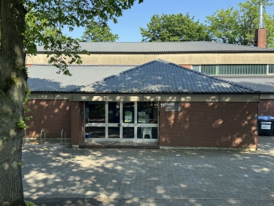 Außenansicht auf die Sporthalle Ludgeri-Schule. Die Eingangstür und der Vorraum zur Sporthalle. Im Vordergrund ein Parkplatz und Fahrradständer.